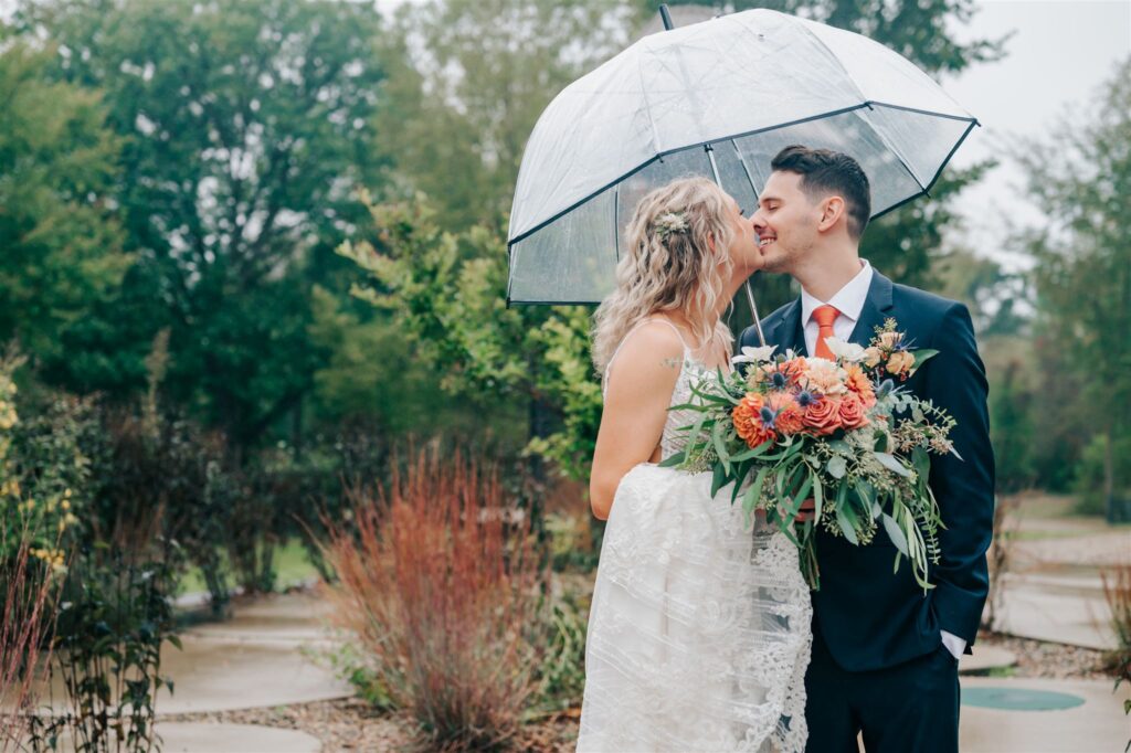 Bride and groom under an umbrella kissing at Robin Hills Farm in Chelsea Michigan